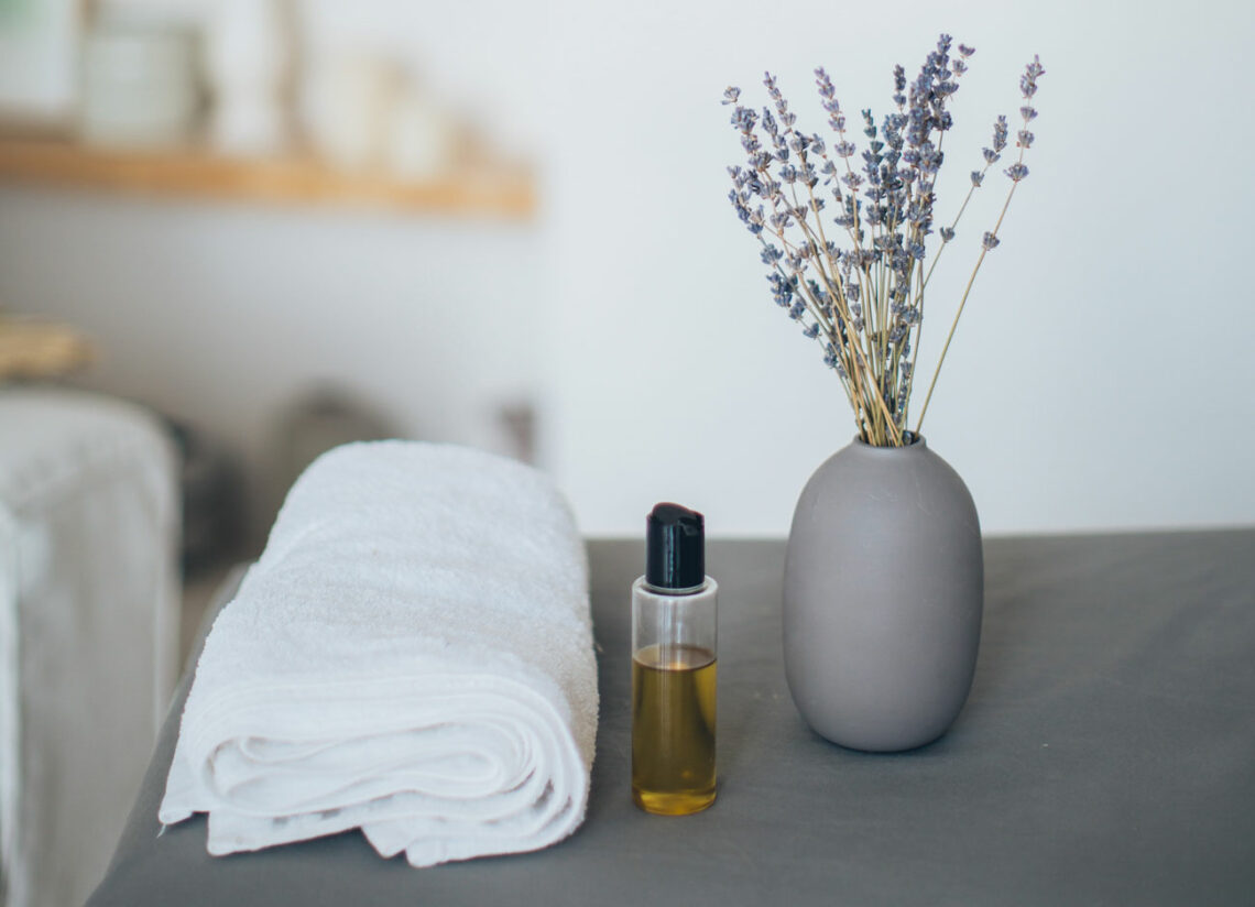 Lavendelöl mit einer Lavendelpflanze neben einem Handtuch