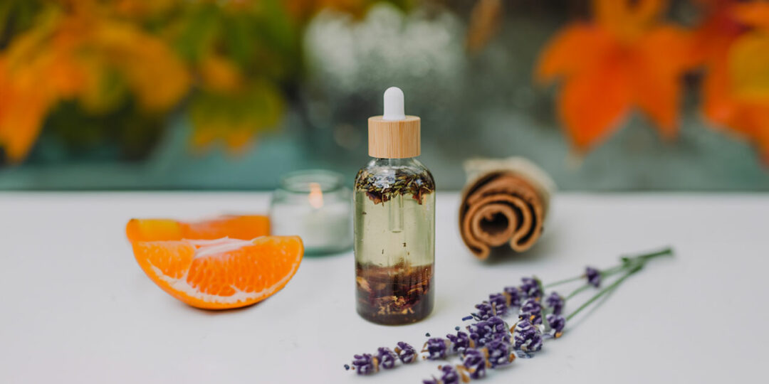 Selbstgemachtes ätherisches Herbstöl mit einer Zimtstange, Lavendel und einer Mandarine im Hintergrund