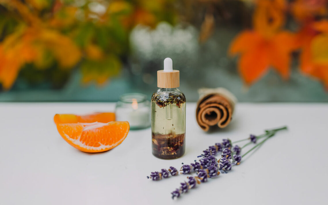Selbstgemachtes ätherisches Herbstöl mit einer Zimtstange, Lavendel und einer Mandarine im Hintergrund