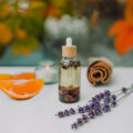 Selbstgemachtes ätherisches Herbstöl mit einer Zimtstange, Lavendel und einer Mandarine im Hintergrund